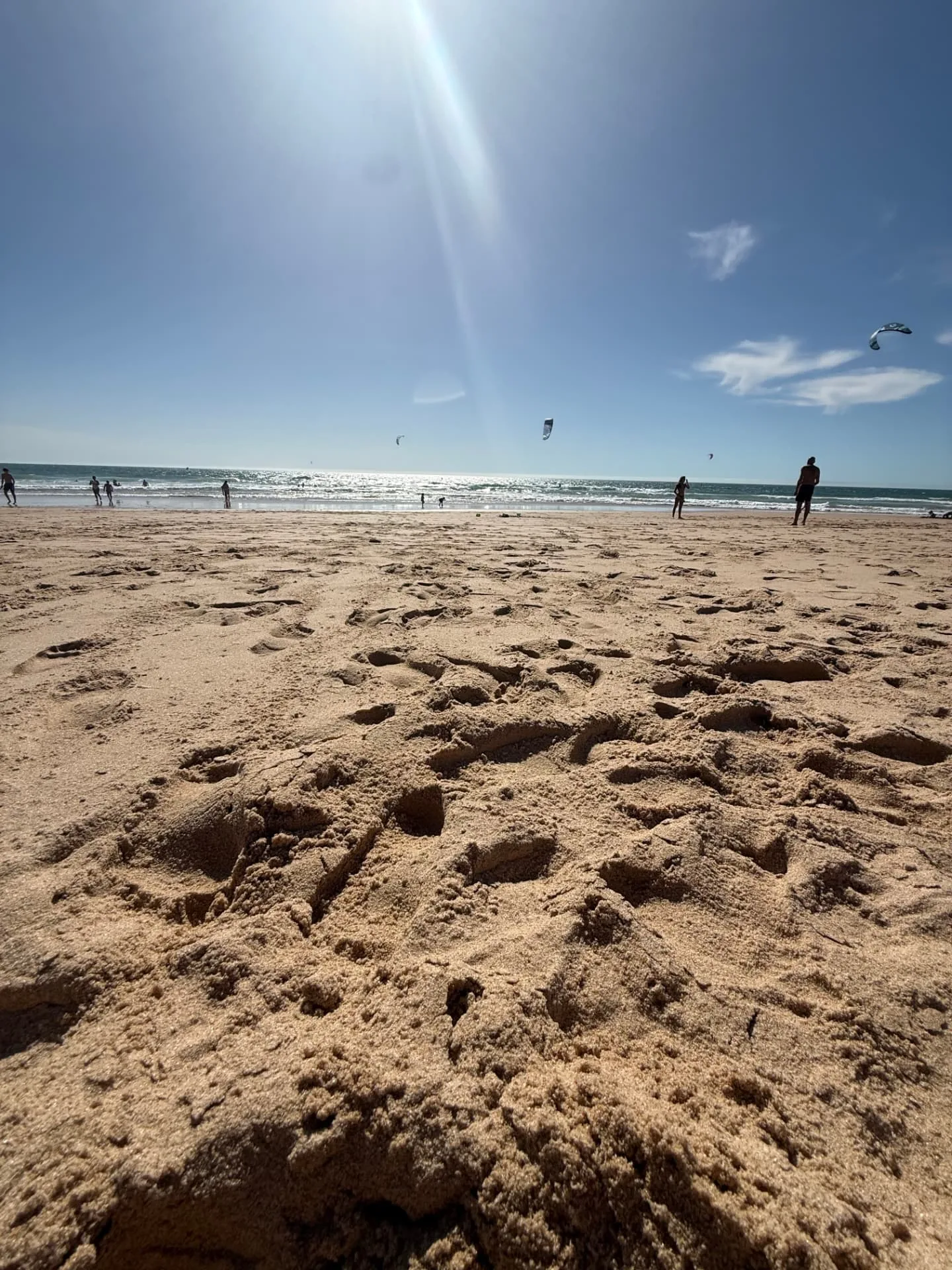 Wide sandy Atlantic beach with kitesurfers beneath a clear blue sky