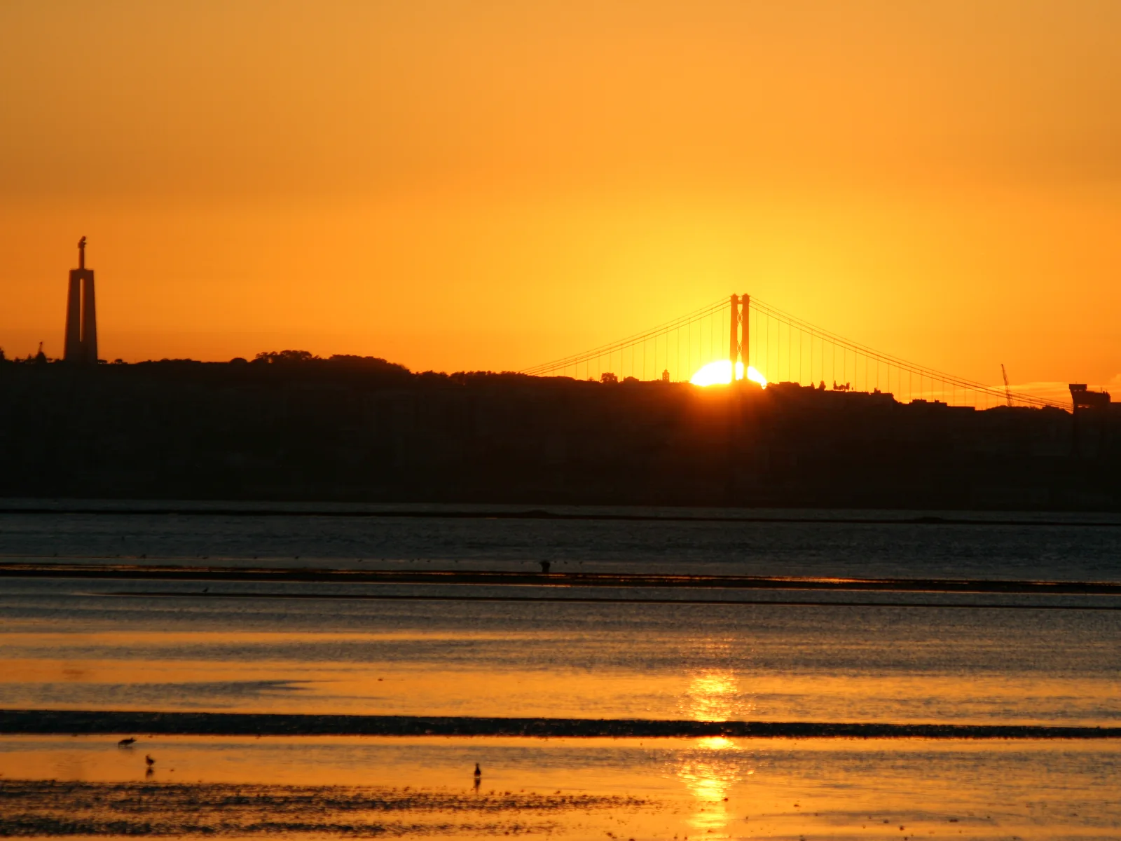 Cristo Rei and the 25 de Abril Bridge silhouetted above the Tagus at sunset in Almada, Portugal