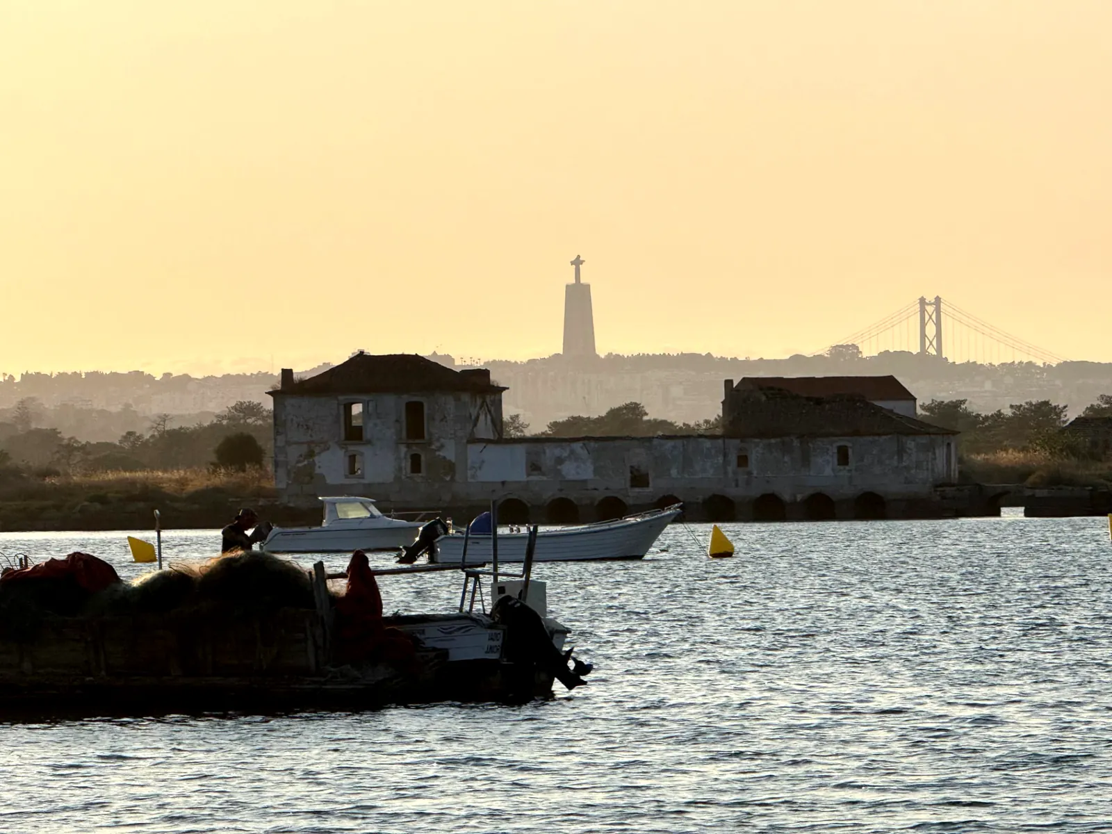Old tide mill on the water at dusk, with Cristo Rei and the 25 de Abril Bridge on the skyline