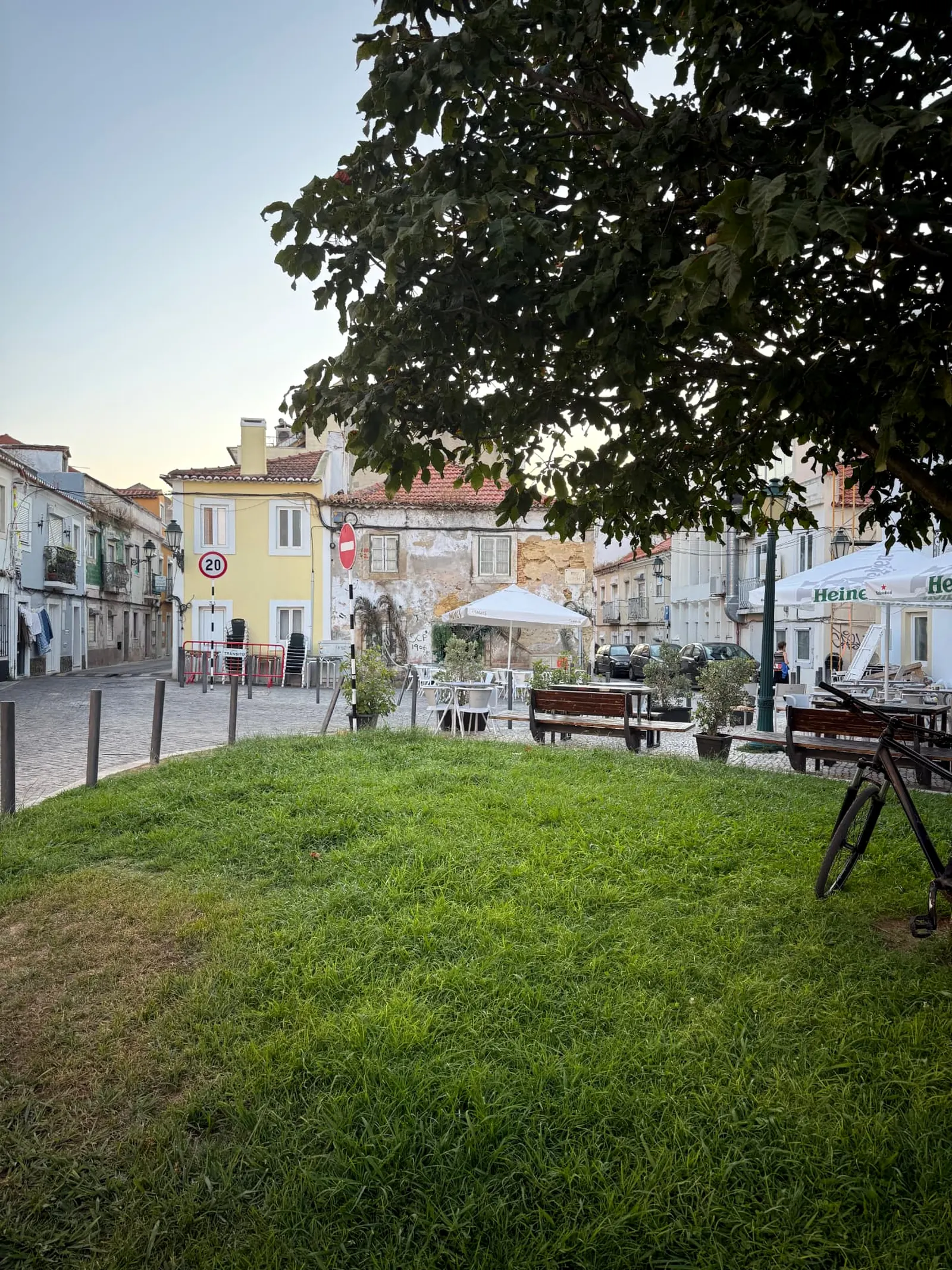 Small tree-shaded square with café tables and pastel houses in Almada’s older streets