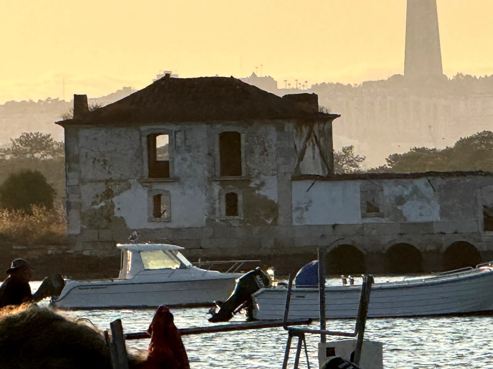 Weathered riverside tide-mill building and moored boats in golden evening haze