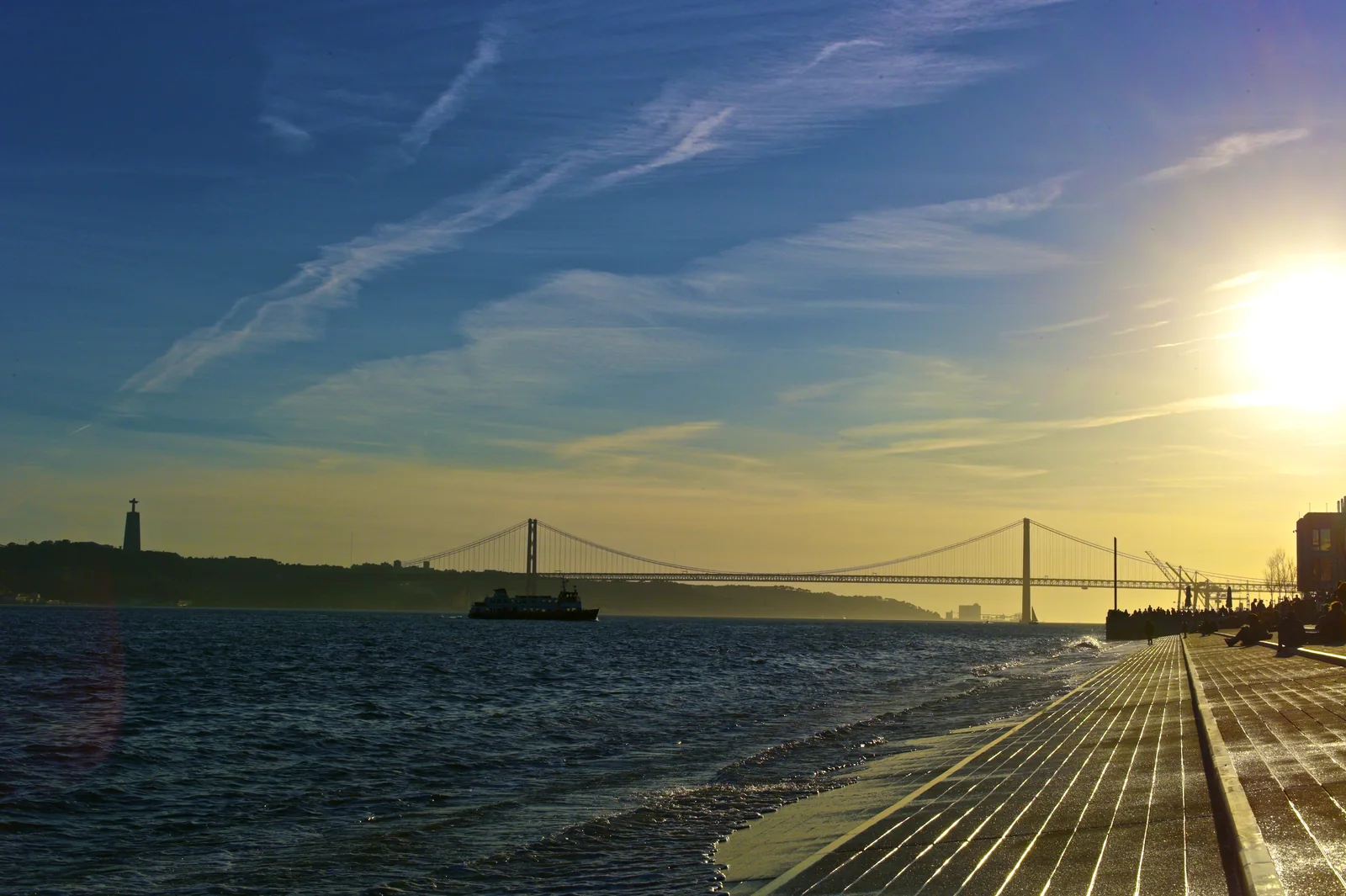 Ferry crossing the Tagus at golden hour with the 25 de Abril Bridge and Cristo Rei beyond
